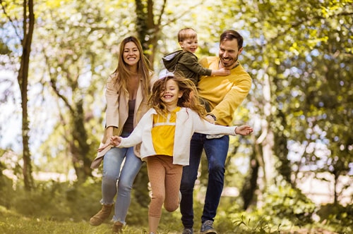 A mom and dad walk happily through a wooded area with their two children
